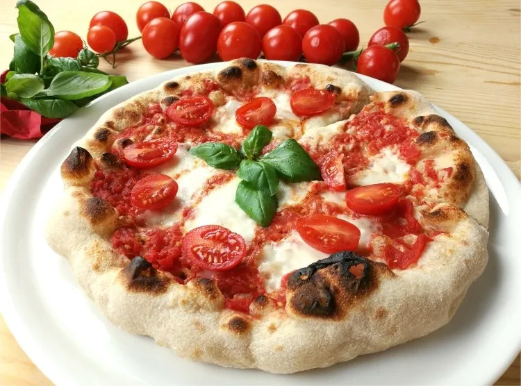 Pizza margherita napoletana appena sfornata, con pomodorini e basilico, su un piatto bianco